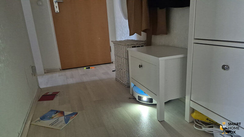 Der Dreame L50 Pro Ultra navigiert mit abgesenktem Laserturm unter einem niedrigen Möbelstück.